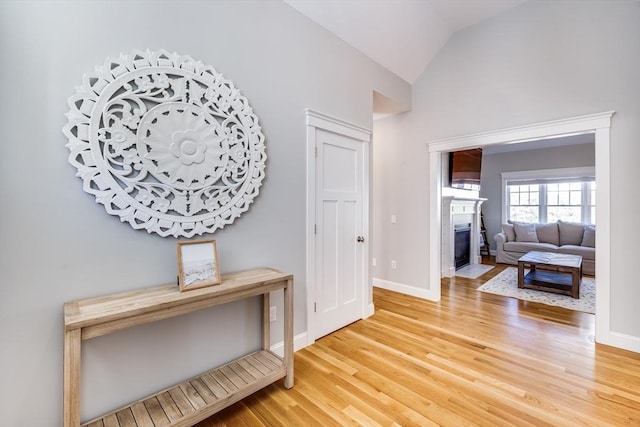 hall featuring wood finished floors, lofted ceiling, and baseboards