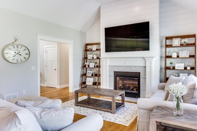 living area featuring lofted ceiling, light wood-style floors, a fireplace with flush hearth, and baseboards