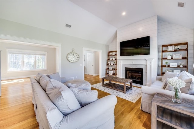 living area featuring vaulted ceiling, light wood-style floors, a high end fireplace, and baseboards