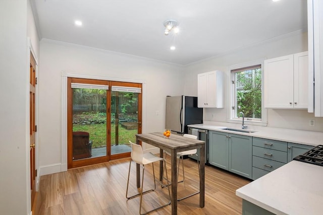 kitchen with a sink, appliances with stainless steel finishes, white cabinetry, light countertops, and ornamental molding