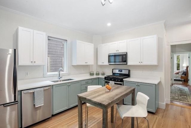 kitchen featuring stainless steel appliances, a sink, light wood-style floors, white cabinets, and crown molding