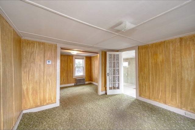 spare room featuring carpet flooring, wooden walls, and radiator