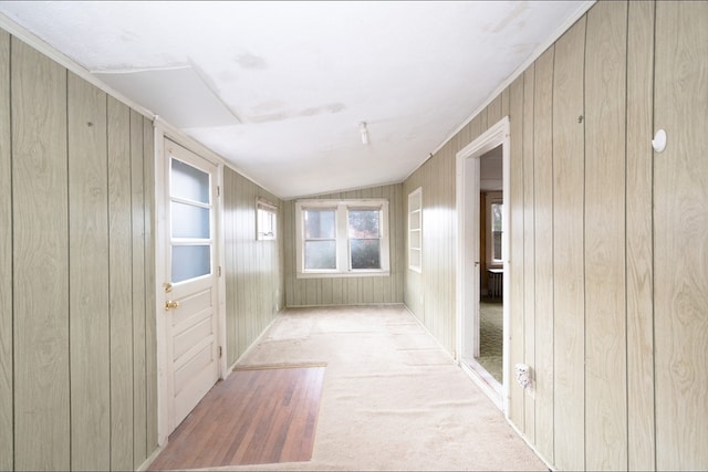 hall featuring wooden walls, vaulted ceiling, and light carpet