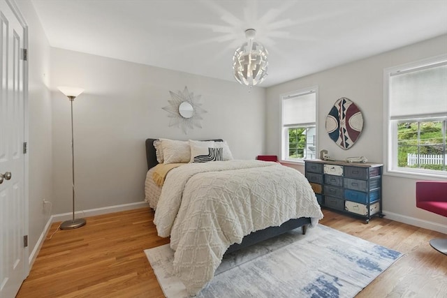 bedroom with light wood finished floors, multiple windows, baseboards, and an inviting chandelier