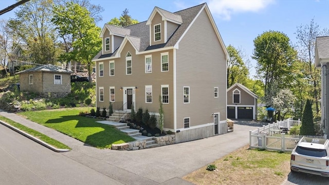 view of home's exterior featuring roof with shingles, fence, a detached garage, an outdoor structure, and a yard
