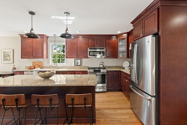kitchen featuring reddish brown cabinets, stainless steel appliances, pendant lighting, and a kitchen bar