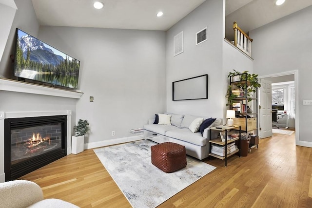 living area with recessed lighting, baseboards, visible vents, a glass covered fireplace, and wood finished floors