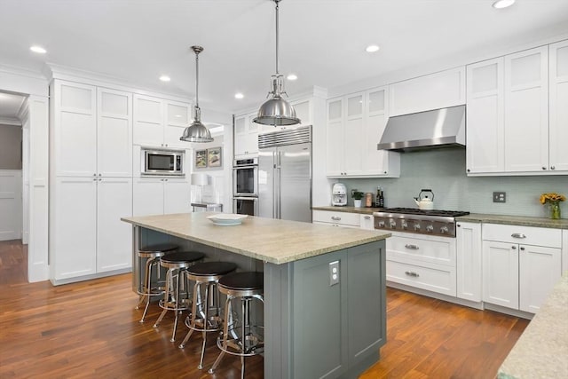 kitchen featuring built in appliances, wall chimney range hood, white cabinetry, a kitchen island, and backsplash