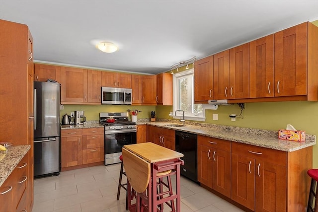 kitchen featuring light tile patterned floors, light stone counters, brown cabinets, stainless steel appliances, and a sink