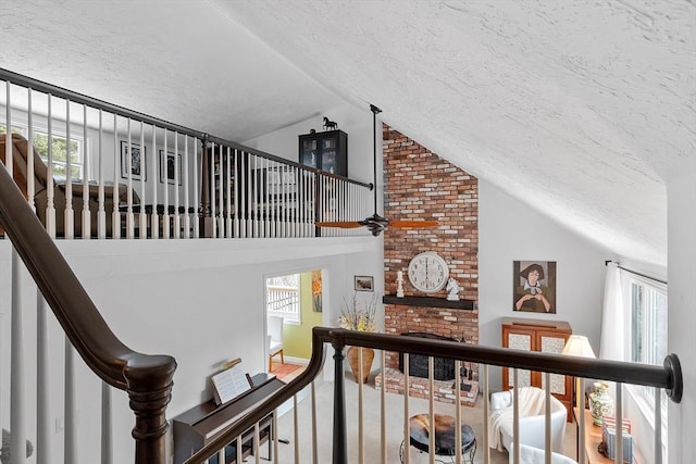 stairway with a ceiling fan, lofted ceiling, a fireplace, and a textured ceiling