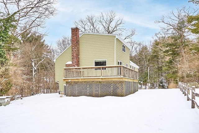 snow covered house with a chimney and a wooden deck