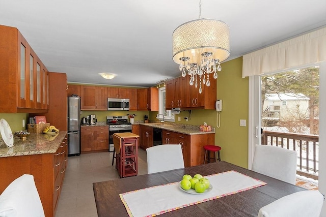 kitchen featuring light tile patterned floors, brown cabinetry, a sink, stainless steel appliances, and a notable chandelier