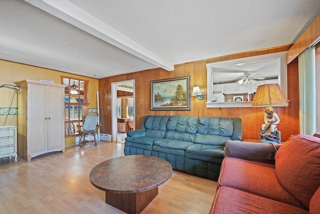 living room with a textured ceiling, wood walls, light wood-type flooring, ceiling fan, and beam ceiling