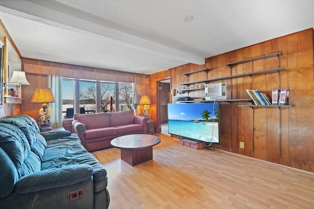 living room featuring beamed ceiling, wood walls, light hardwood / wood-style floors, and a textured ceiling