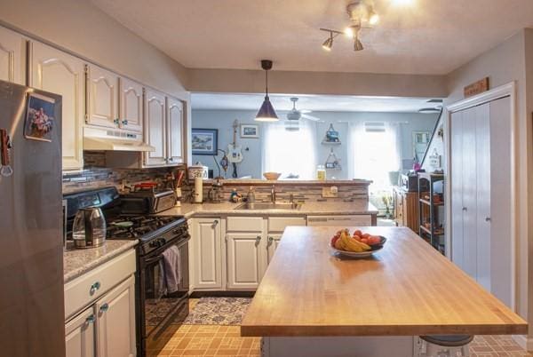 kitchen with black range with gas cooktop, under cabinet range hood, a sink, freestanding refrigerator, and a peninsula
