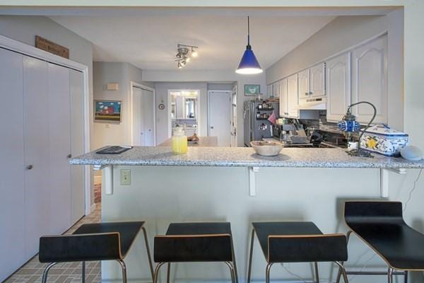 kitchen with a peninsula, a breakfast bar area, freestanding refrigerator, and white cabinetry