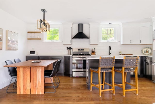 108 Central St, Ipswich, MA 01938 - kitchen with wall chimney range hood, stainless steel range with gas cooktop, a center island, white cabinets, and a breakfast bar area