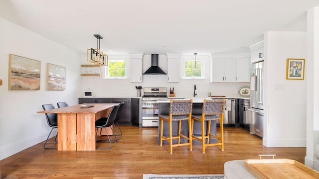 108 Central St, Ipswich, MA 01938 - kitchen with appliances with stainless steel finishes, wall chimney range hood, a breakfast bar, white cabinetry, and light countertops