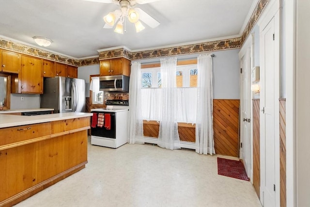 kitchen featuring ceiling fan, baseboard heating, appliances with stainless steel finishes, and wood walls