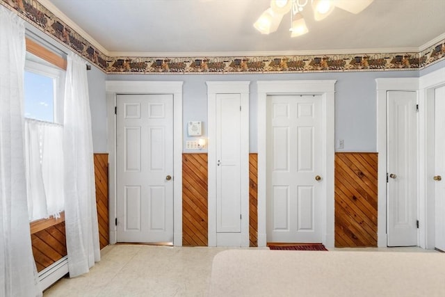 unfurnished bedroom with a baseboard heating unit, ceiling fan, ornamental molding, and wood walls