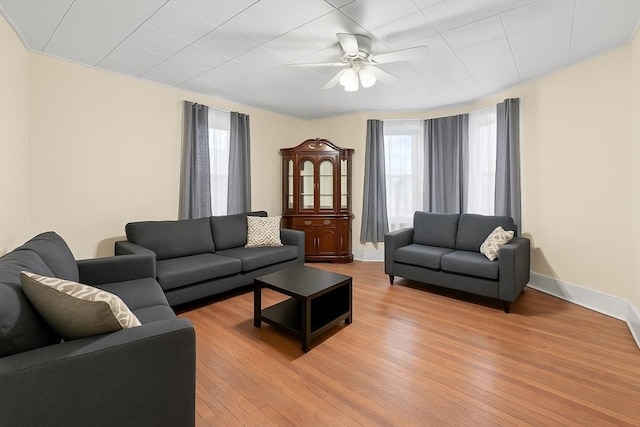 living area with a ceiling fan, light wood-style flooring, and baseboards