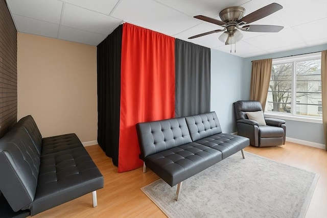 living area with wood finished floors, a ceiling fan, baseboards, and a drop ceiling