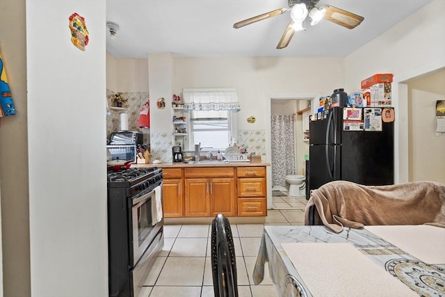 kitchen featuring freestanding refrigerator, stainless steel gas stove, light tile patterned flooring, ceiling fan, and light countertops