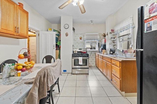kitchen with stainless steel gas range oven, freestanding refrigerator, a sink, ceiling fan, and light tile patterned floors