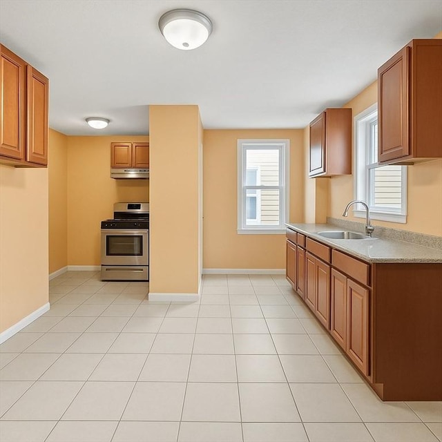 kitchen with gas stove, a sink, light countertops, under cabinet range hood, and brown cabinets