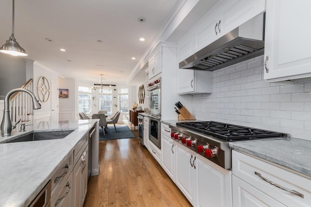 kitchen featuring wall chimney exhaust hood, white cabinetry, pendant lighting, and a sink