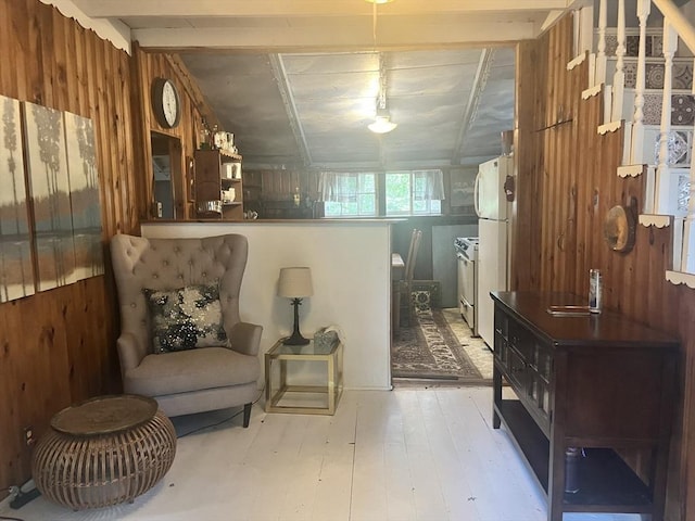 sitting room featuring lofted ceiling with beams, light wood-type flooring, and wooden walls