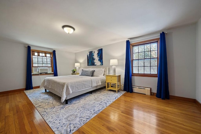 bedroom featuring baseboards, light wood finished floors, a baseboard heating unit, and multiple windows