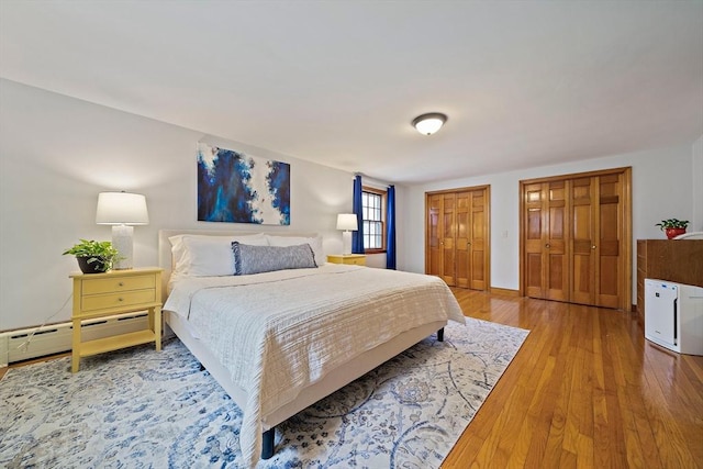 bedroom with multiple closets, a baseboard radiator, wood-type flooring, and baseboards