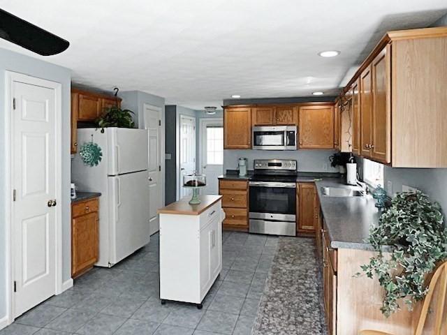 21 Parlee St, Salem, MA 01970 - kitchen with appliances with stainless steel finishes, a center island, light tile patterned flooring, brown cabinetry, and recessed lighting