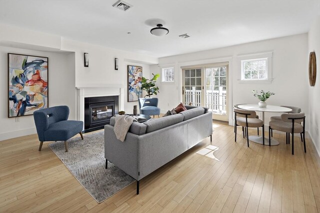 living room featuring visible vents, a fireplace with flush hearth, baseboards, and light wood-style flooring