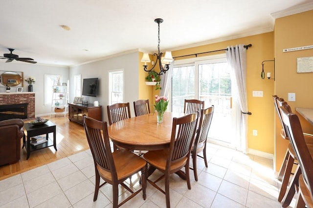 tiled dining area with a brick fireplace, ceiling fan with notable chandelier, and ornamental molding