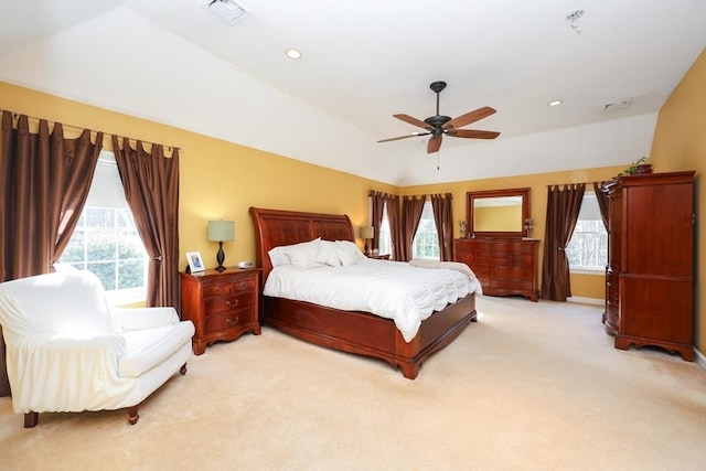 bedroom featuring ceiling fan, light colored carpet, a tray ceiling, and multiple windows