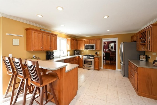 kitchen with sink, appliances with stainless steel finishes, a kitchen breakfast bar, ornamental molding, and kitchen peninsula