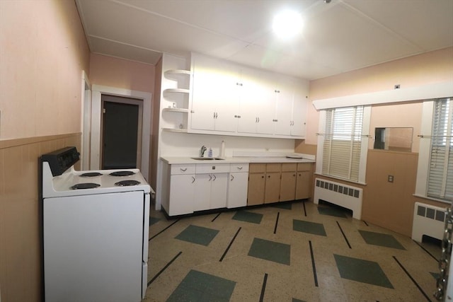 kitchen featuring radiator heating unit, wooden walls, white cabinets, white electric stove, and sink