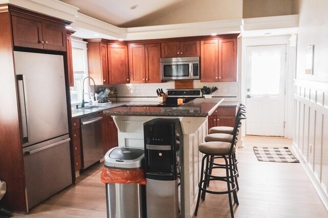 kitchen with appliances with stainless steel finishes, a sink, light wood finished floors, a center island, and decorative backsplash