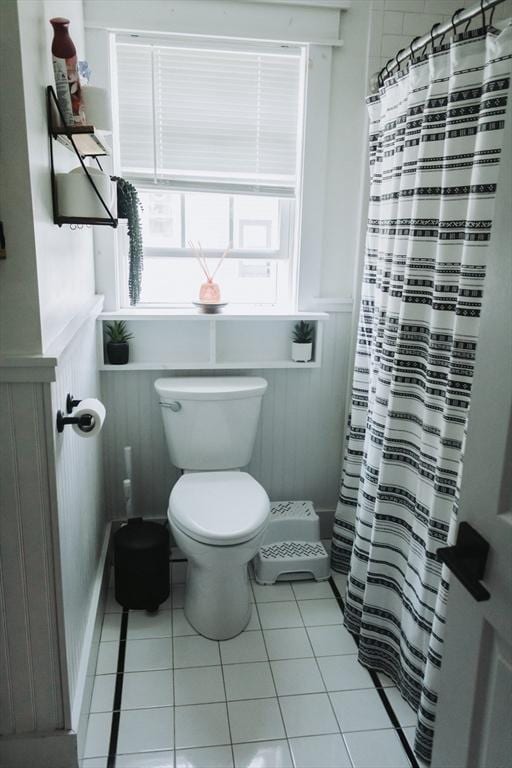 bathroom with plenty of natural light, a wainscoted wall, tile patterned flooring, toilet, and a shower with shower curtain