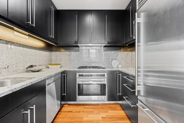 kitchen with light wood finished floors, appliances with stainless steel finishes, decorative backsplash, and dark cabinets