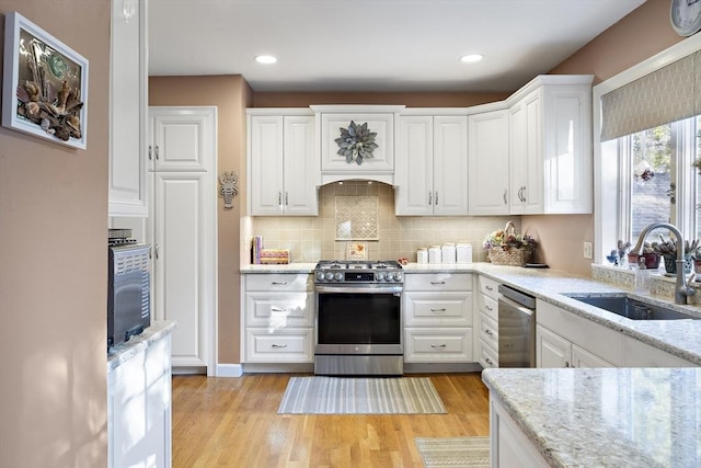 kitchen with sink, white cabinetry, light stone counters, appliances with stainless steel finishes, and light hardwood / wood-style floors