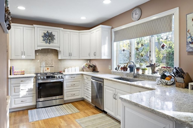 kitchen with sink, white cabinetry, stainless steel appliances, light stone countertops, and light wood-type flooring