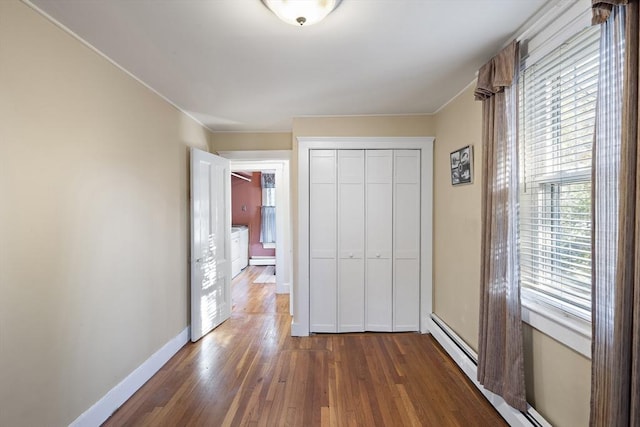 unfurnished bedroom with dark wood-type flooring, multiple windows, baseboard heating, and a closet