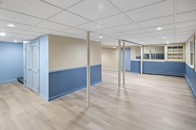 basement with a baseboard radiator, a paneled ceiling, and hardwood / wood-style floors