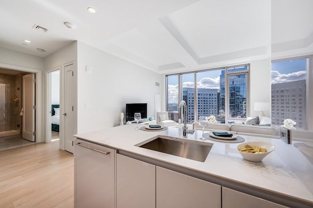 kitchen featuring light wood-type flooring, white cabinetry, expansive windows, and sink