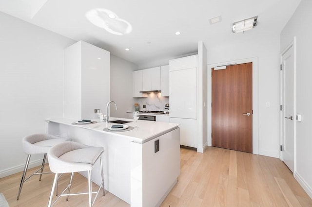 kitchen with kitchen peninsula, sink, light hardwood / wood-style flooring, white cabinets, and stainless steel gas stovetop