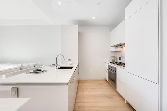 kitchen featuring sink, light hardwood / wood-style flooring, appliances with stainless steel finishes, white cabinetry, and kitchen peninsula