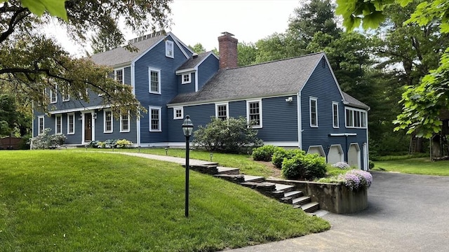 view of front of house featuring a front lawn, a chimney, an attached garage, and aphalt driveway